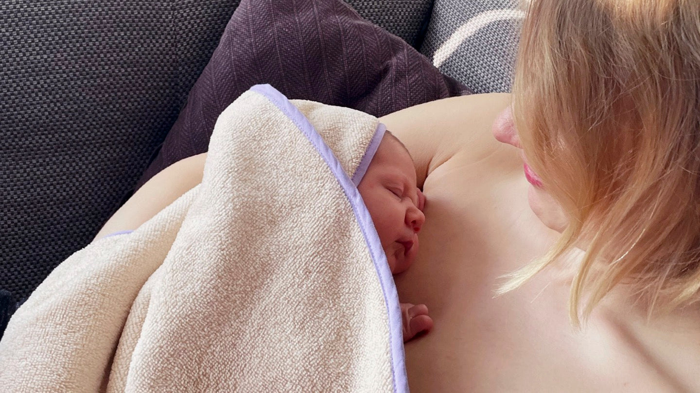Baby mit Bonding-Cape liegt auf der nackten Brust seiner Mutter